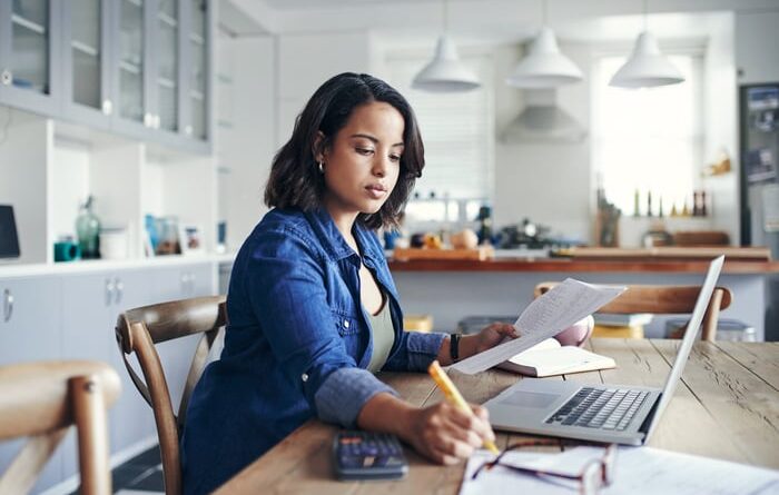 A serious person in the kitchen, holding a document and a notepad.